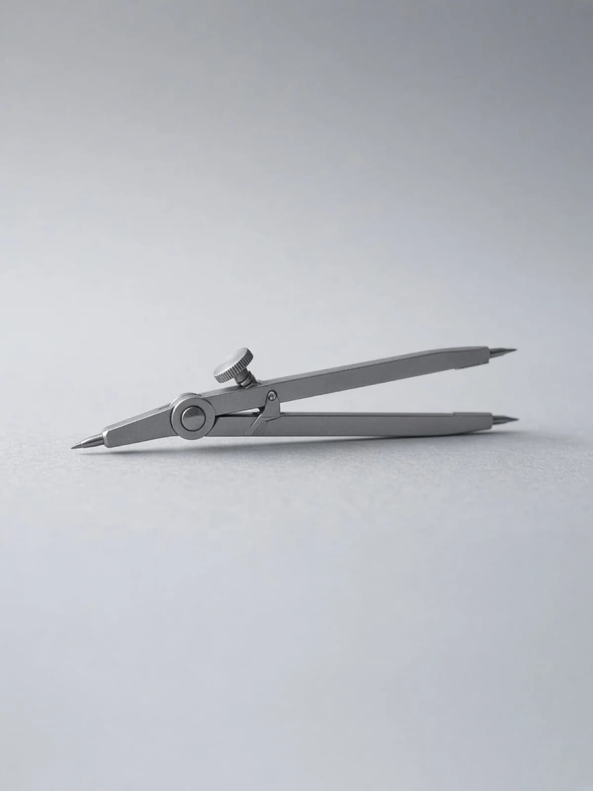A steel drafting compass lying on its side on a desk