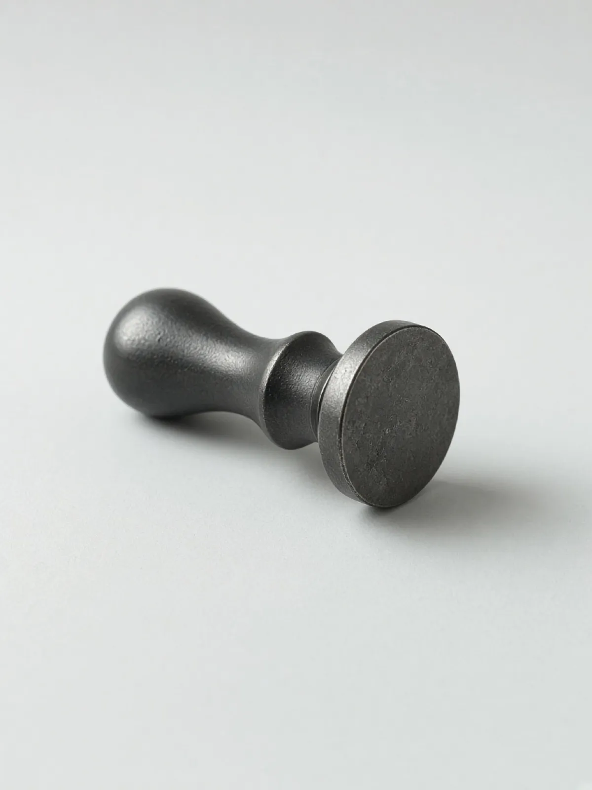A pewter wax-seal stamp lying on its side on a desk