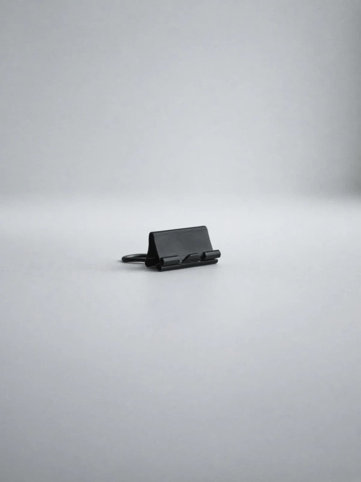A black metal binder clip lying on its side on a desk