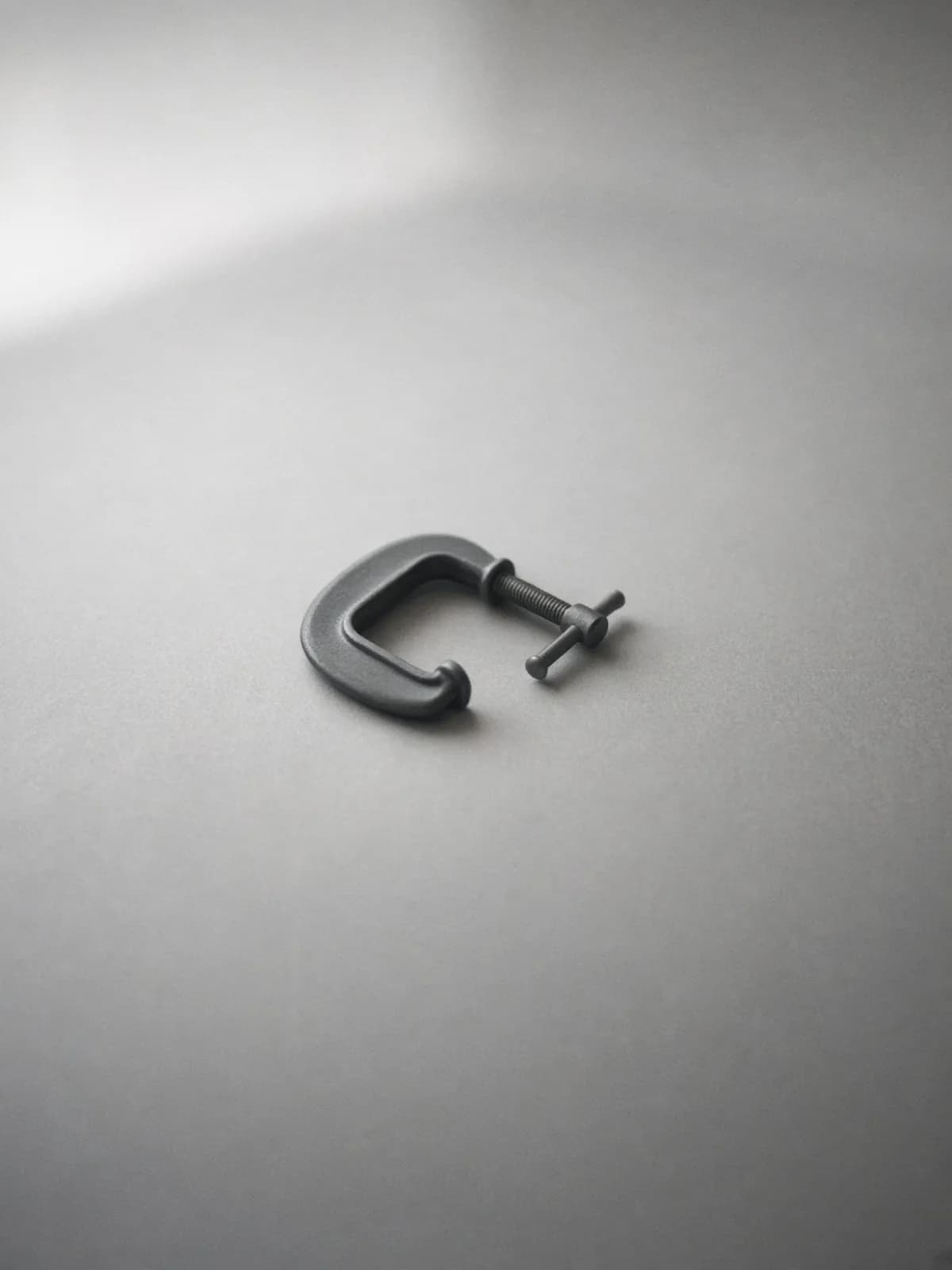 A small steel C-clamp lying on its side on a desk