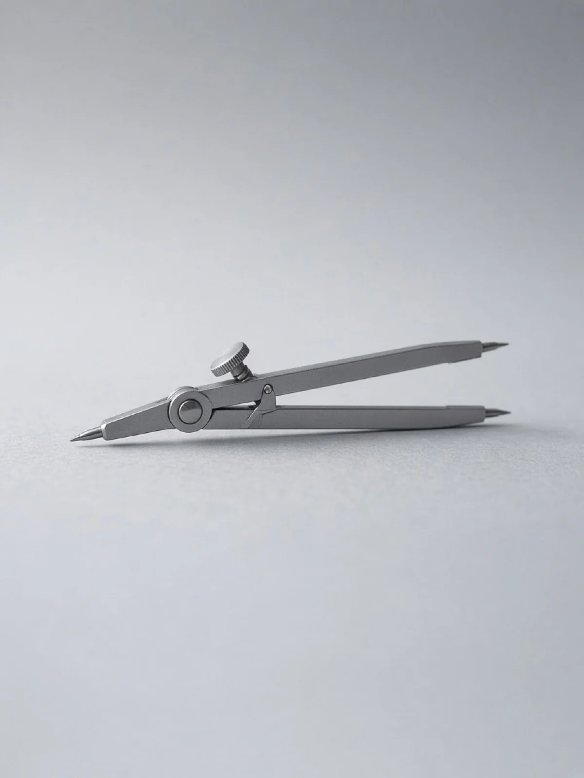 A steel drafting compass lying on its side on a desk