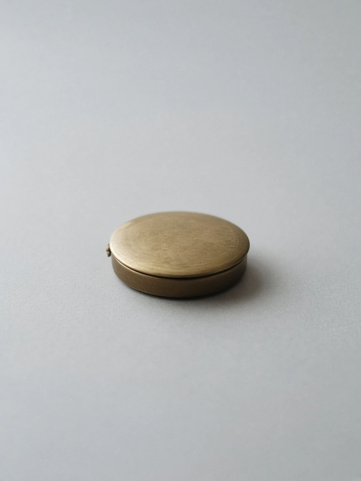 A closed brass pocket watch lying on its side on a desk