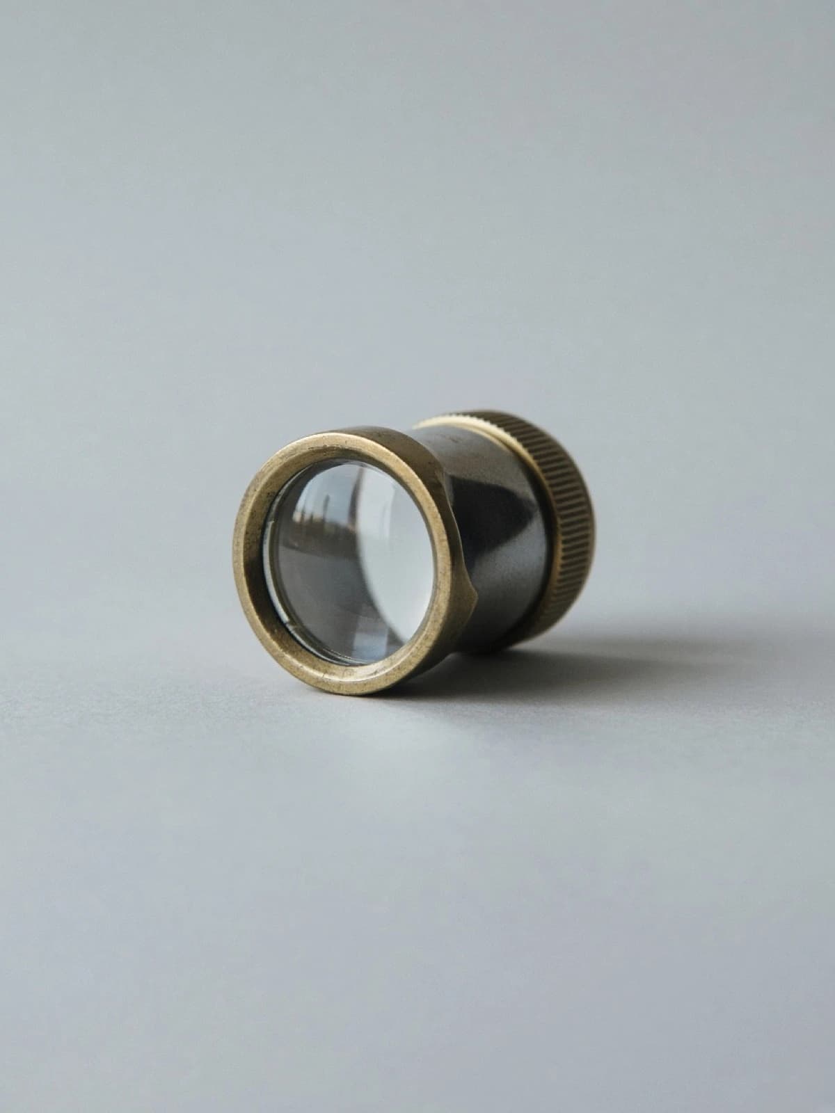 A brass jeweler's loupe lying on its side on a desk