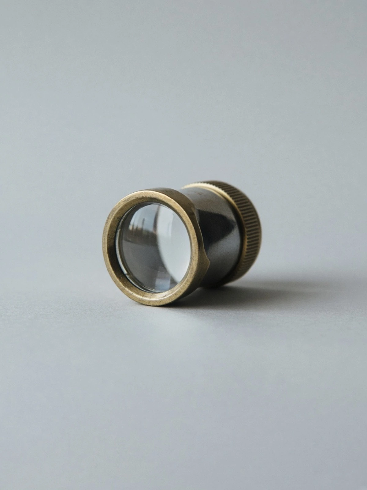 A brass jeweler's loupe lying on its side on a desk