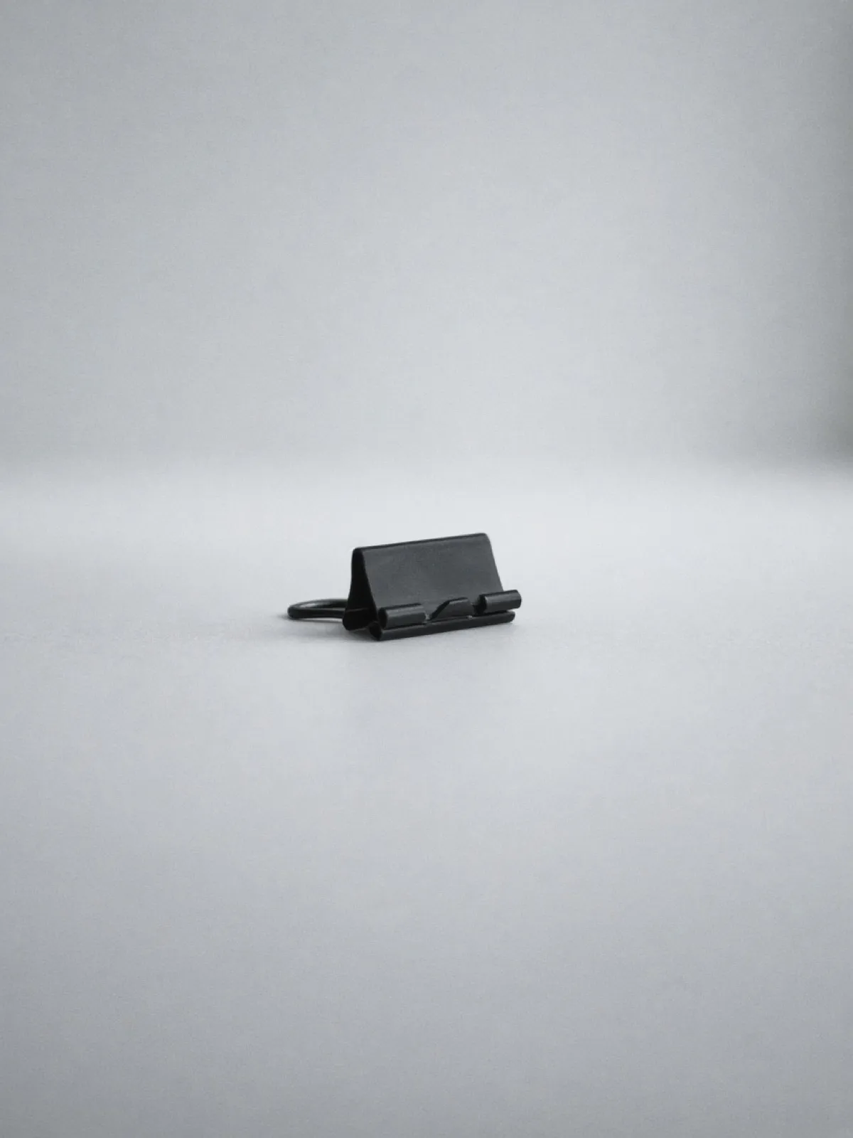 A black metal binder clip lying on its side on a desk