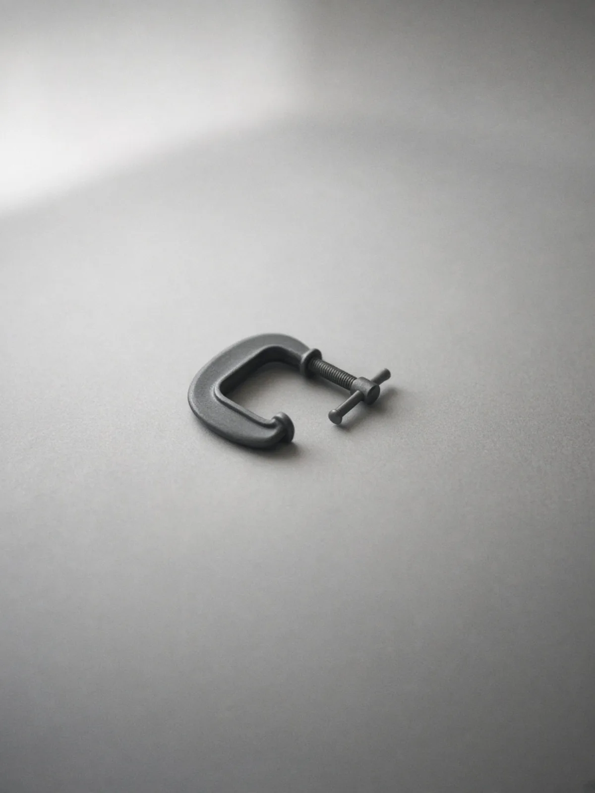 A small steel C-clamp lying on its side on a desk
